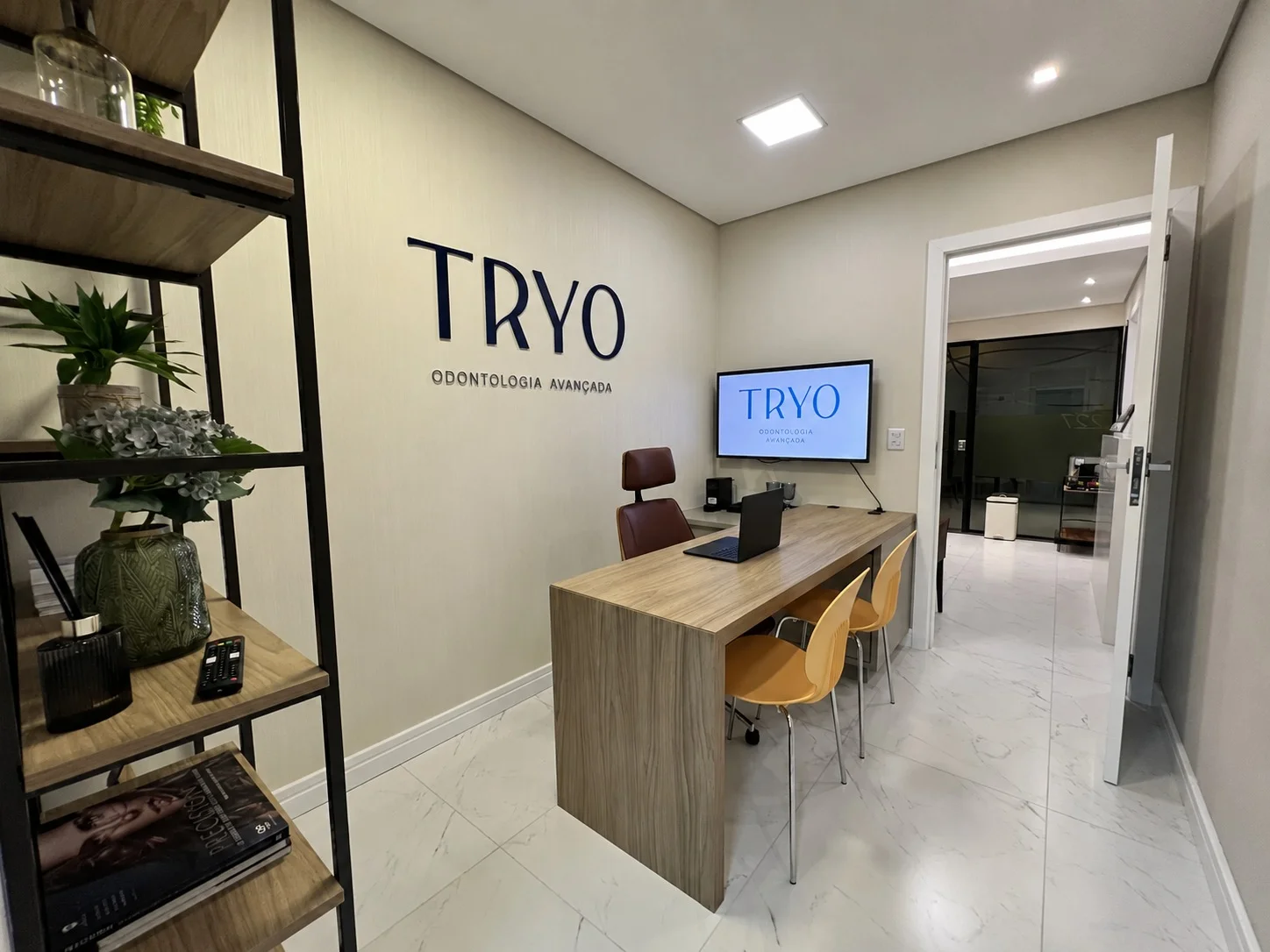 Sala de planejamento da Tryo, com a logo Tryo na parede e exibida na tela, estante de apoio e mesa de trabalho
